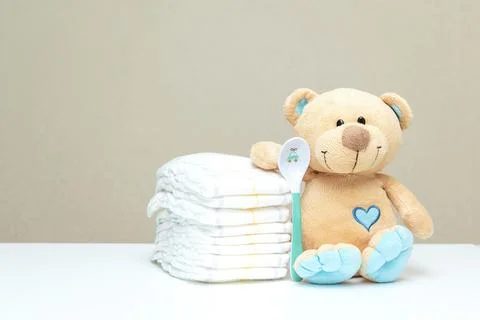 Stack of diapers with toy teddy bear with spoon on table. set for baby show.. Foto stock