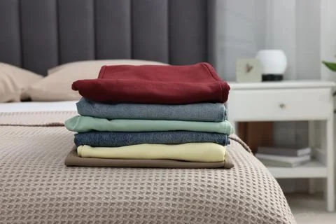 Stack of different folded clothes on bed at home Stock Photos