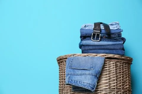Stack of different jeans on basket against color wall with space for text Foto stock