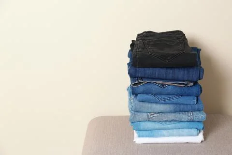 Stack of different jeans on ottoman against light background. Space for text Foto stock