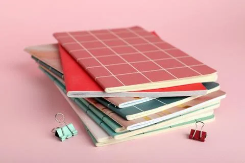Stack of different notebooks with binder clips on pink background Stock Photos