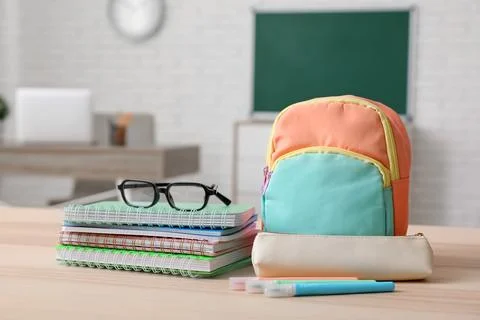 Stack of different notebooks with eyeglasses and backpack on wooden desk in c Stock Photos