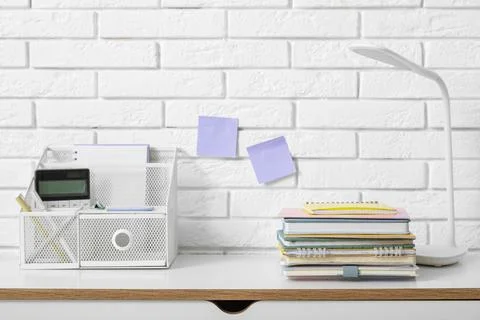 Stack of different notebooks with stationery holder and lamp on table near wh Stock Photos