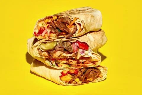 A stack of different shawarma with meat, vegetables and falafel on a yellow b Stock Photos
