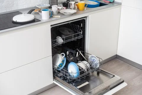 A stack of dirty dishes is on the door of the dishwasher. Stock Photos