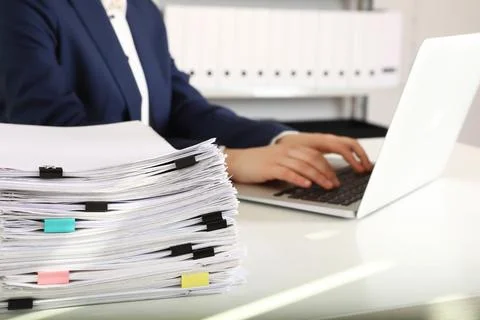 Stack of documents and woman working with laptop at table in office, closeup 스톡 사진