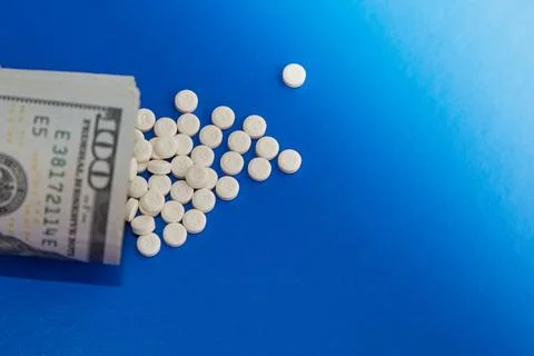 A stack of dollar bills and white pills on the blue surface of a table close- Stock Photos