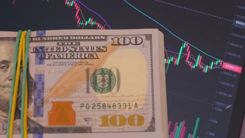 A stack of dollars lies on the tablet screen with a running chart of the Stock Footage 234337031