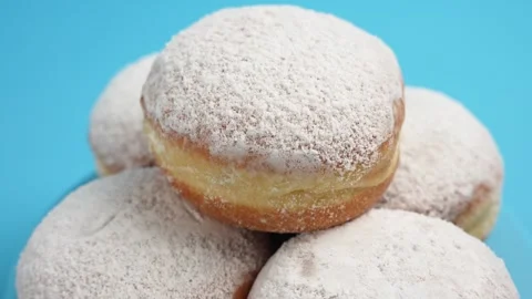 A stack of donuts in powdered sugar are rotating on a blue background. Stock Footage 303594829