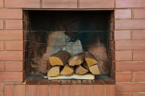 A stack of dry firewood in a red clay brick fireplace in a country cottage Stock Photos