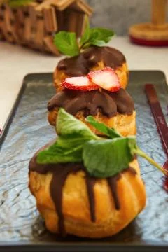 Stack eclair of profiteroles with dark melted chocolate on a black dish. Stock Photos