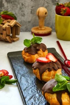 Stack eclair of profiteroles with dark melted chocolate on a black dish. Stock Photos