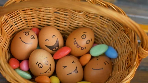 Stack of eggs with hand drawn faces on straw basket with colorful candy, easter Video stock 153138374