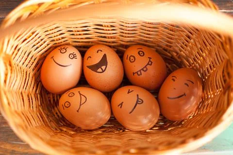Stack of eggs with hand drawn faces on straw basket, easter preparation, holiday Stock Photos
