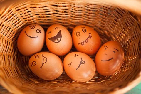 Stack of eggs with hand drawn faces on straw basket, easter preparation, holiday Stock Photos