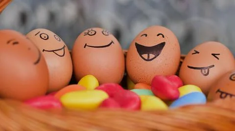 Stack of eggs with hand drawn faces on straw basket with colorful candy, easter Stock Photos