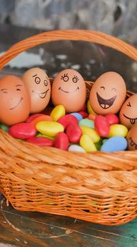 Stack of eggs with hand drawn faces on straw basket with colorful candy, easter Stock Photos