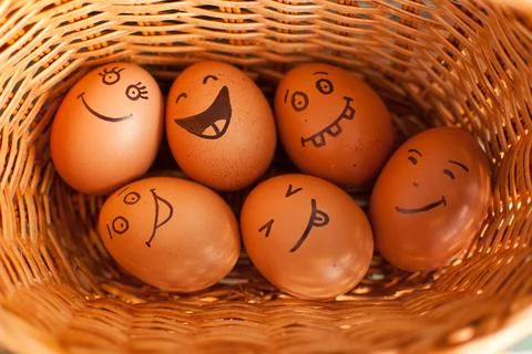Stack of eggs with hand drawn faces on straw basket, easter preparation, holiday Stock Photos