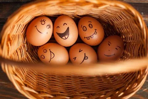 Stack of eggs with hand drawn faces on straw basket, easter preparation, holiday Stock Photos