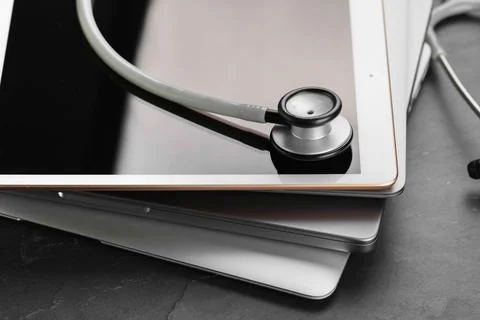 Stack of electronic devices and stethoscope on black table, closeup 库存照片