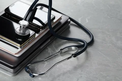 Stack of electronic devices and stethoscope on grey table, closeup 库存照片