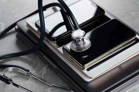 Stack of electronic devices and stethoscope on grey table, closeup Foto stock