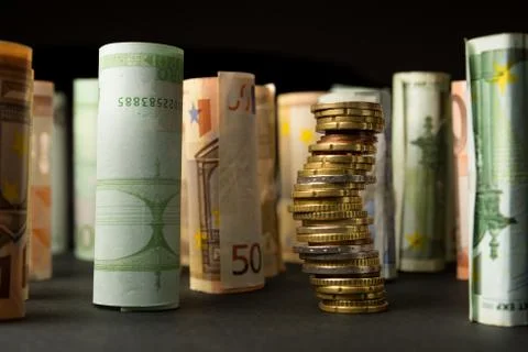 Stack of euro coins and rolls of bank notes in the background Stock Photos