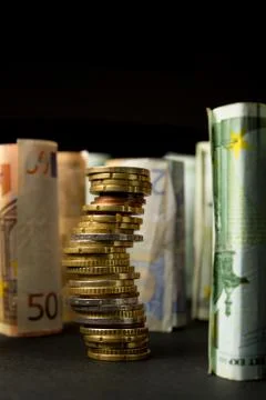 Stack of euro coins and rolls of bank notes in the background Stock Photos