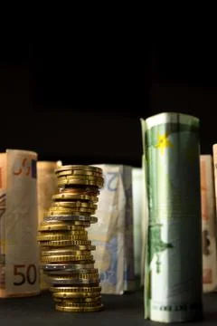 Stack of euro coins and rolls of bank notes in the background Stock Photos