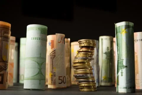 Stack of euro coins and rolls of bank notes in the background Stock Photos