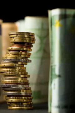 Stack of euro coins and rolls of bank notes in the background Stock Photos