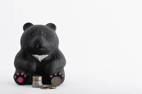A stack of euro coins next to a piggy bank in the form of a black bear made o Stock Photos