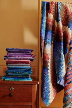 Stack of fabrics and quilt made in the bargello style on yellow wall backgrou Stock Photos
