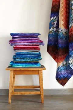 Stack of fabrics on a stool and quilt top made in the bargello style on neu.. Stock-Fotos