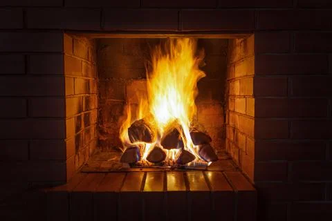 A stack of firewood burns with a bright hot flame in a red brick fireplace on Stock Photos