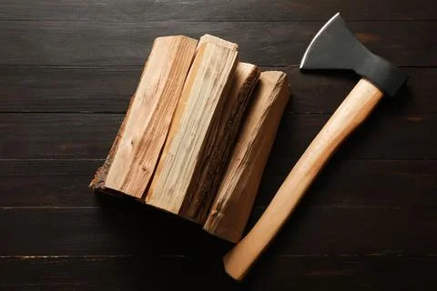 Stack of firewood logs with ax on dark wooden background Stock Photos