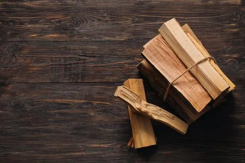 Stack of firewood logs tied with rope on dark wooden background Stock Photos
