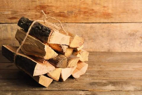 Stack of firewood logs tied with rope on wooden background Stock Photos