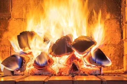 A stack of flaming firewood in a red mud brick fireplace in a country cottage Foto stock