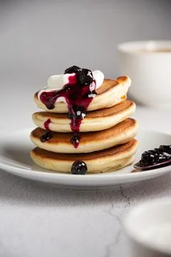 A stack of fluffy pancakes with cream poured with berry jam on a white plate on Stock Photos