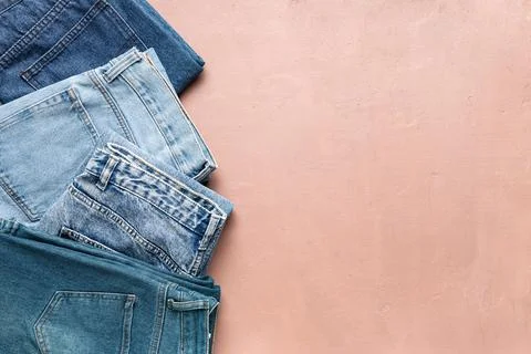 Stack of folded blue denim jeans in various washes on a textured pink backgro Stock Photos