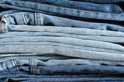 Stack of folded blue denim jeans in various shades, textile background and Fa 库存照片