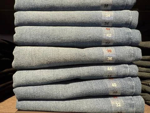 Stack of folded blue jeans in various sizes in retail setting with visible .. Fotos de archivo
