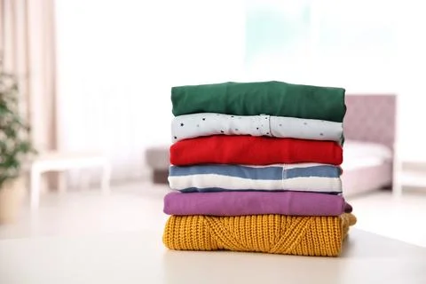 Stack of folded bright clothes on table against blurred background. Space for 库存照片