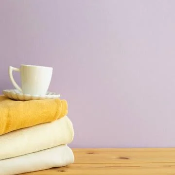 Stack of folded clothes and cup of coffee on wooden table. purple backgrou... 스톡 사진