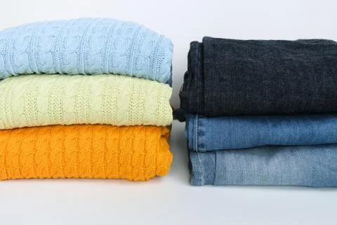 Stack of folded colorful sweater, pullover with blue jeans against white Stock Photos