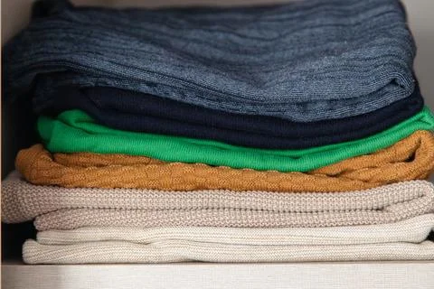 Stack of folded knit sweaters in different colors neatly arranged on a shelf Foto stock