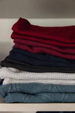 Stack of folded knit sweaters in different colors neatly arranged on a shelf Stock Photos