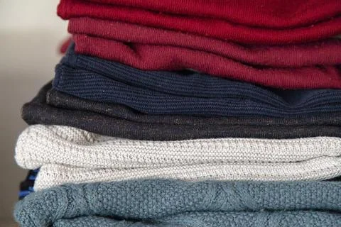 Stack of folded knit sweaters in different colors neatly arranged on a shelf Foto stock