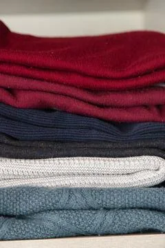 Stack of folded knit sweaters in different colors neatly arranged on a shelf Stock Photos